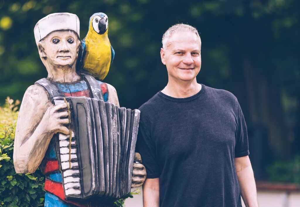 Stephan Creifelds von Klicklab - Porträt neben einer Figur, die Akkordion spielt und einen Papagei auf der Schulter hat